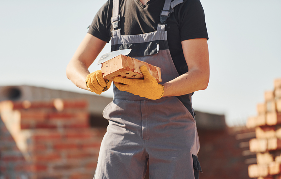 Holds brick in hands. Construction worker in uniform and safety equipment have job on building Imatge d'un obrer de Porta Gastó, construcció rehabilitació i instal·lacions integrals.